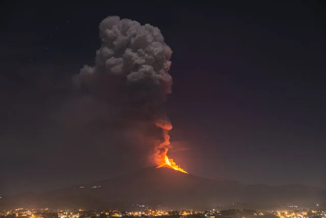 Flames and smoke billowing from a crater, as seen from the southern side of the Mt Etna volcano, tower over the city of Pedara, Sicily, Wednesday night, February 24, 2021. Europe's most active volcano has been steadily erupting since last week, belching smoke, ash, and fountains of red-hot lava. (Photo by Salvatore Allegra/AP Photo)