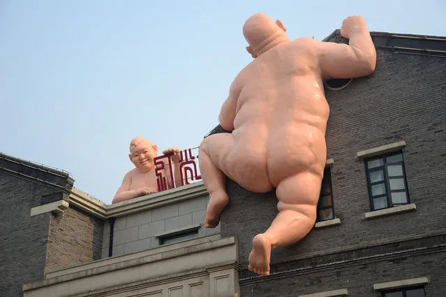 One of two naked sculptures is seen on the rooftop of a house in Jinan city, east Chinas Shandong province, 20 December 2015. Two naked sculptures climbed on wall in Jinan, capital of east China's Shandong Province, on Sunday. A previous version of the naked sculpture was demolished soon after it went viral on Chinese social media in 2014. (Photo by Imaginechina/Splash News)