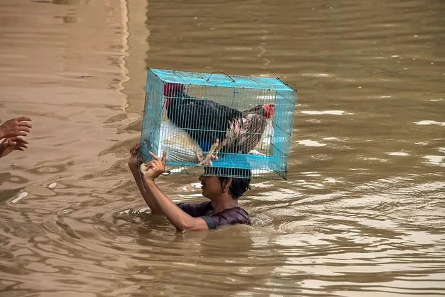 A person carries chickens in a cage on his head through flooded streets in New Delhi, India, on Friday, July 14, 2023. (Photo by Anindito Mukherjee/Bloomberg)