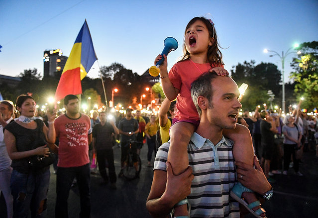 People take part in an anti government protest in front of the Government headquarters in Bucharest on August 12, 2018. Thousands gathered Sunday in Romania's capital for a third night of protest against the government after Friday's mass demonstration left hundreds injured. Singing the national anthem and waving national flags, protesters again amassed at Victory Square in front of the government headquarters in Bucharest. (Photo by Daniel Mihailescu/AFP Photo)