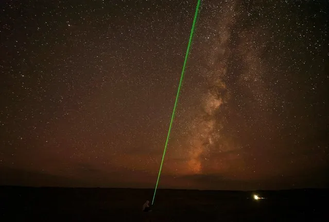 A man uses laser light towards the sky as the Milky Way galaxy is seen in the sky around camp in the natural reserve area of Wadi Al-Hitan, or the Valley of the Whales, at the desert of Al Fayoum Governorate, southwest of Cairo at the desert of Al Fayoum, Egypt on August 12, 2023. (Photo by Mohamed Abd El Ghany/Reuters)
