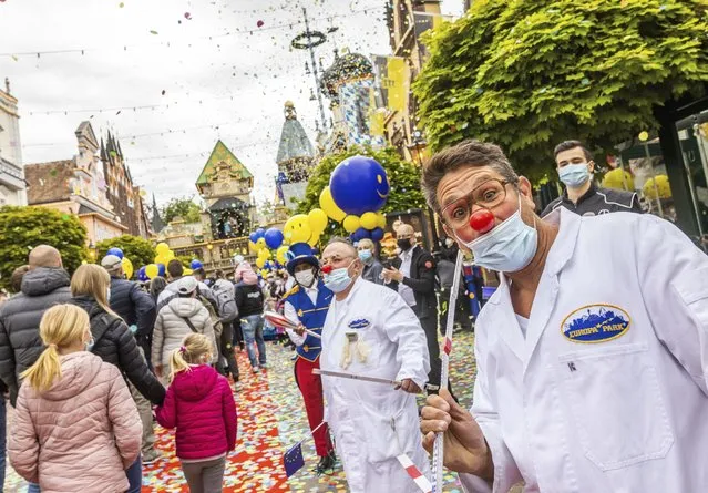 Visitors of Europa-Park walk through an avenue at the entrance of the park while employees of the park stand guard and confetti rains down from confetti cannons in Rust, Germany, Friday, May 21, 2021. Europa-Park is one of the first major theme parks in Germany to reopen its doors to visitors. The park in Rust welcomed visitors again after months of the Corona enforced break – as part of a model project approved by the state. (Photo by Philipp von Ditfurth/dpa via AP Photo)