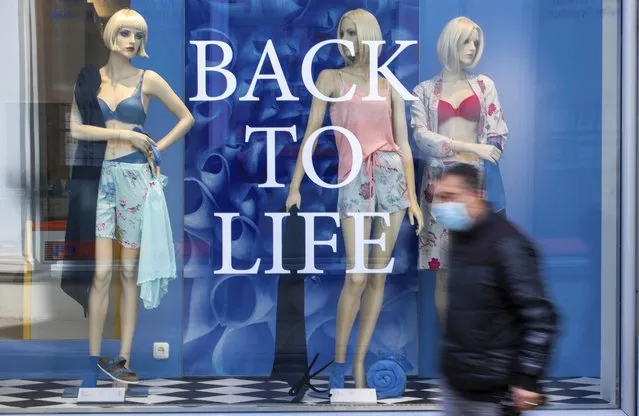 A man wearing a mouth-nose protection to protect against the coronavirus walks past a department store window with the words “BACK TO LIFE” in Schwerin, Germany, Thursday, April 15, 2021. (Photo by Jens Buettner/dpa via AP Photo)