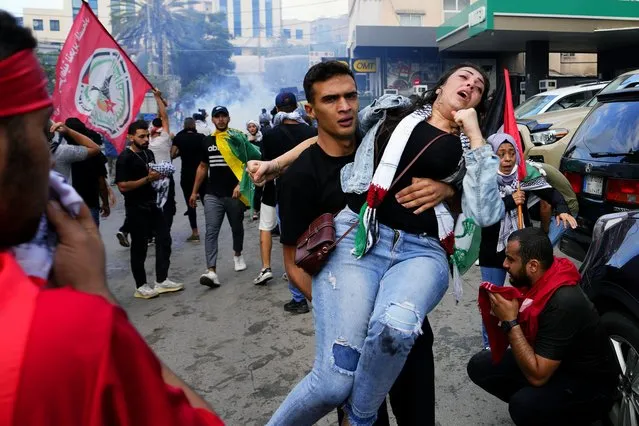 A protester carries an injured woman during a demonstration in solidarity with the Palestinian people in Gaza, near the U.S. embassy in Aukar, a northern suburb of Beirut, Lebanon, Wednesday, October 18, 2023. (Photo by Hassan Ammar/AP Photo)