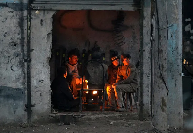 People warm themselves around a fire inside a shop in the Syrian rebel-held town of al-Rai, Syria January 9, 2017. (Photo by Khalil Ashawi/Reuters)