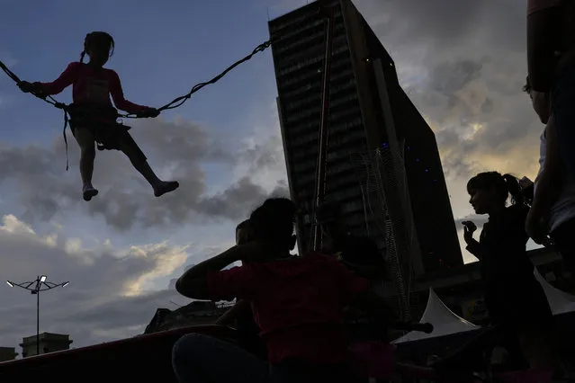 A girl wearing a protective harness jumps on a trampoline as other children wait their turn at Plaza Caracas in Caracas, Venezuela, Sunday, September 24, 2023. (Photo by Matias Delacroix/AP Photo)