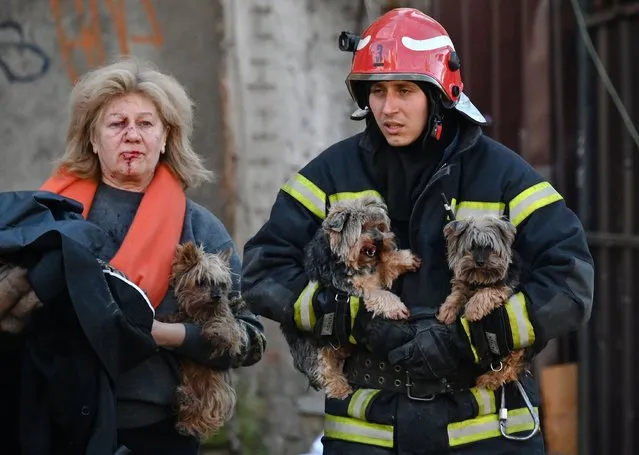 An emergency worker carries dogs as he escorts a local resident outside a partially destroyed multistorey office building after several Russian strikes hit the Ukrainian capital of Kyiv on October 10, 2022, amid Russia's invasion of Ukraine. The head of the Ukrainian military said that Russian forces launched at least 75 missiles at Ukraine on Monday morning, with fatal strikes targeting the capital Kyiv, and cities in the south and west. (Photo by Sergei Supinsky/AFP Photo)