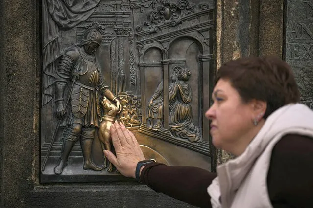 A woman touches a bronze plaque below the statue of Saint John of Nepomuk on Charles Bridge in Prague, Czech Republic, Friday, November 11, 2022. Touching the two bronze plaques below the statue, said to bring good luck, is very popular among tourists visiting the Czech capital. (Photo by Vadim Ghirda/AP Photo)
