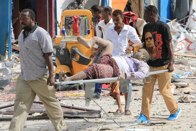 Somali men carry a civilian who was wounded in a suicide car bomb attack on a hotel in Mogadishu, Somalia, Wednesday, January 25, 2017. Gunmen from Somalia's violent Islamic extremist rebels fought their way into a hotel in the Somali capital after a suicide car bomb exploded at its gates, a police officer said Wednesday. (Photo by Farah Abdi Warsameh/AP Photo)