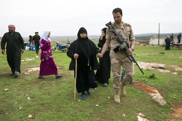 In this photo taken on Wednesday, March 2, 2016, a Syrian solder helps an elderly woman as she comes to receive humanitarian aid from Russian military near Maarzaf, about 15 kilometers west of Hama, Syria.  Associated Press spent five days traveling through the port of Latakia and the surrounding areas in Syria during the cease-fire. (Photo by Pavel Golovkin/AP Photo)
