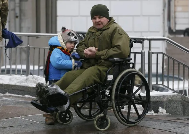 A wheelchair-bound man and a child attend a funeral ceremony for the seven Ukrainian servicemen, who were recently killed during a military conflict in the east of the country, in central Kiev, Ukraine, February 1, 2017. (Photo by Valentyn Ogirenko/Reuters)