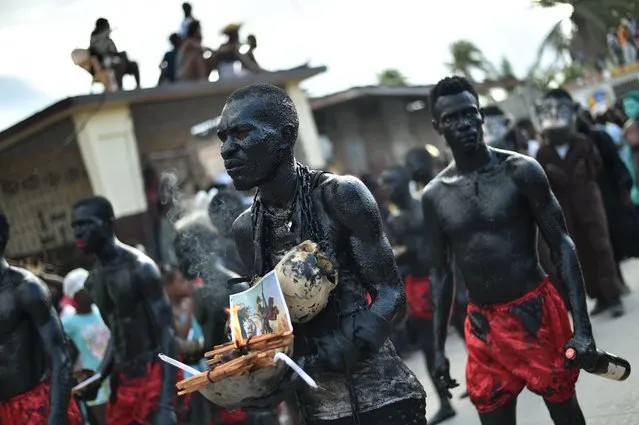 A reveler carrying skulls walks with his band with body painted with a mixture of cane sugar and coal, perform during of 2017 National Carnival Parade on February 26, 2017, in the city of Les Cayes, southwest Haiti. The name of the carnival for this year is “Tet ansanb pou gran sid leve kanpe”, in Haitian creole, (together for the South to rise up) Last year 546 people died and more than 175,000 people lost their homes when Hurricane Matthew roared ashore on October 4, packing 230- kilometer- per- hour winds in Haiti. Food, medicine and other essential aids took time to reach the areas struck by Hurricane Matthew. (Photo by Hector Retamal/AFP Photo)