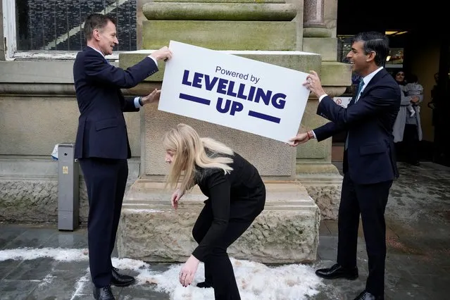 Britain's Prime Minister Rishi Sunak (R) and Chancellor of the Exchequer Jeremy Hunt hold a “Levelling Up” plaque as local MP Sara Britcliffe (C) walks past during a visit to Accrington Market Hall on January 19, 2023. (Photo by Christopher Furlong/Pool via AFP Photo)
