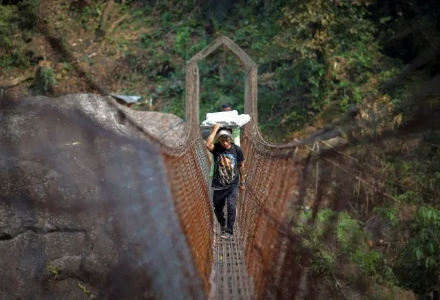 Cornelius Mawa, 28, a porter, carries Voter Verifiable Paper Audit Trail (VVPAT) and Electronic Voting Machines (EVM) as he crosses a suspension bridge to reach a remote polling station, ahead of the first phase of the election, in Shillong in the northeastern state of Meghalaya, India, on April 17, 2024. (Photo by Adnan Abidi/Reuters)