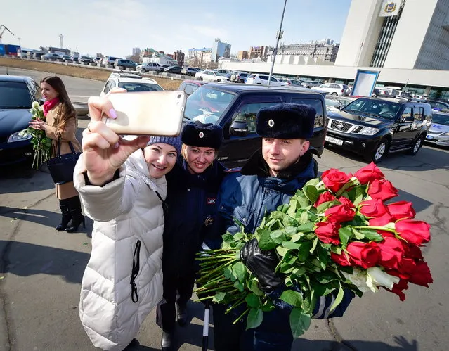A female driver takes a selfie with traffic policemen who have congratulated her on upcoming International Women's Day in the citys Central Square in Vladivostok, Russia on March 7, 2017. Policemen in several Russian cities pulled over women on Tuesday and Wednesday, which is International Women’s Day – but instead of writing tickets, they handed out roses. March 8 is similar to Valentine’s Day in Russia, and it has become a day dedicated to buying women flowers and pampering them. Photos capture quite the spectrum of reactions. (Photo by Yuri Smityuk/TASS via Getty Images)