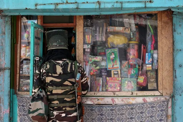 An Indian security force personnel buys goods from a shop during restrictions after the scrapping of the special constitutional status for Kashmir by the government, in Srinagar, August 13, 2019. (Photo by Danish Ismail/Reuters)