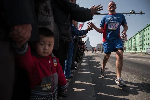 Competitors of the Pyongyang Marathon run past spectators, before the Ryugyong hotel (rear C) in central Pyongyang on April 9, 2017. Hundreds of foreigners lined up in Pyongyang's Kim Il-Sung Stadium on Sunday ahead of the Pyongyang Marathon, the highlight of the isolated country's annual tourism calendar. (Photo by Ed Jones/AFP Photo)