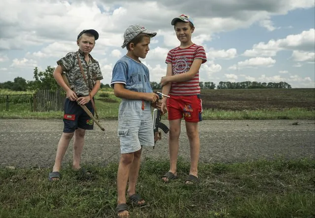 Local children holding toy guns stand at the site of the crashed Malaysia Airlines Flight 17 plane, near the village of Hrabove, eastern Ukraine, Thursday, July 16, 2015. A year since a Malaysia Airlines Boeing 777 was blown out of the sky over war-ravaged eastern Ukraine, killing 298 people, there has been little official word of progress in determining what brought down Flight MH17. (Photo by Mstyslav Chernov/AP Photo)