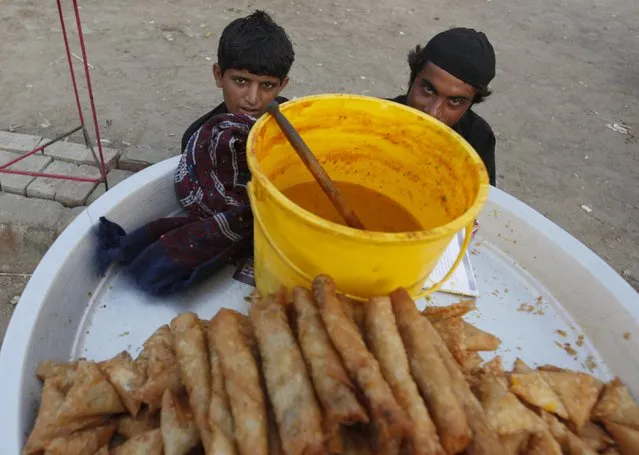 Boys sit while selling vegetable rolls and samosas along a street in Karachi, Pakistan, April 22, 2016. (Photo by Akhtar Soomro/Reuters)