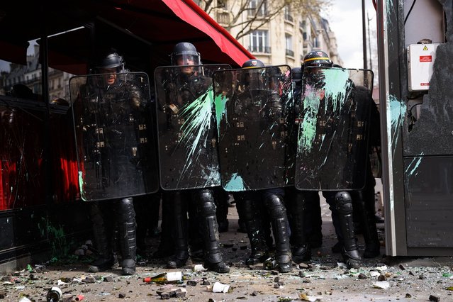 French CRS riot police shield themselves from projectiles and paint as they form a cordon around the “La Rotonde” brasserie restaurant during clashes with protesters on the sidelines of a demonstratoin on the 11th day of action after the government pushed a pensions reform through parliament without a vote, using the article 49.3 of the constitution, in Paris on April 6, 2023. France on April 6, 2023 braced for another day of protests and strikes to denounce French President's pension reform one day after talks between the government and unions ended in deadlock. (Photo by Thomas Samson/AFP Photo)