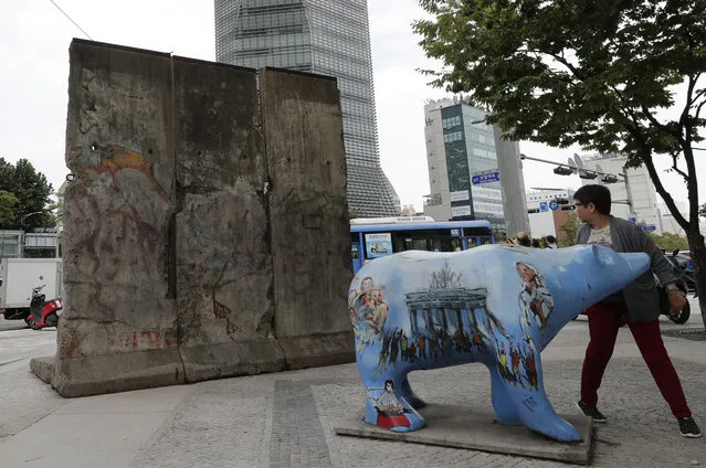 A woman walks near the three sections of the Berlin Wall and the sculpture of the Bear, the symbol of Berlin, near the Cheonggye stream in Seoul, South Korea, Monday, September 2, 2019. (Photo by Lee Jin-man/AP Photo)
