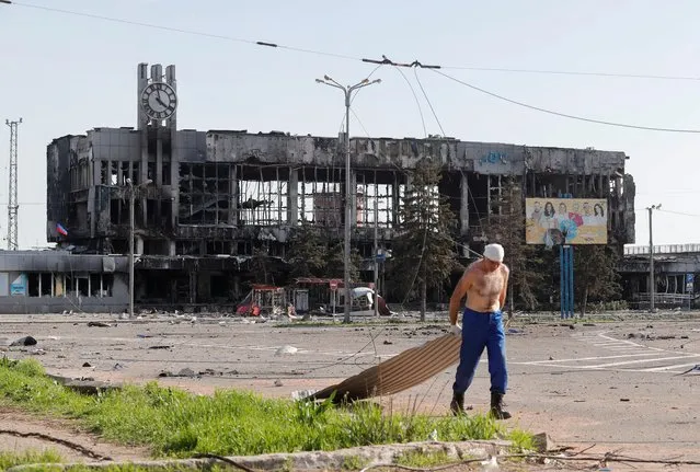 A man drags metal board near a railway station building destroyed during the Ukraine-Russia conflict in the southern port city of Mariupol, Ukraine on April 26, 2022. (Photo by Alexander Ermochenko/Reuters)