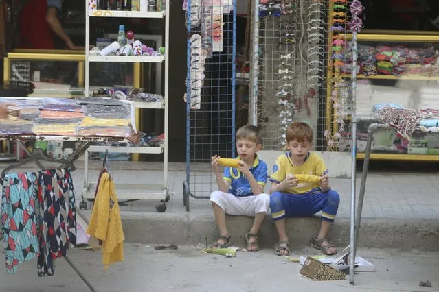 Two boys sit on a pavement as they eat corn in Aleppo's eastern district of Tariq al-Bab, Syria, August 1, 2015. (Photo by Abdalrhman Ismail/Reuters)