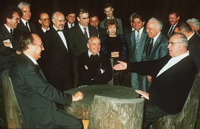 The July 17, 1990 file photo shows Soviet President Mikhail Gorbachev, center,sitting with West German Chancellor Helmut Kohl, right, and German Foreign Minister Hans-Dietrich Genscher at a table in the garden of the guest house in Archiz during a break in their talks on the discussion of NATO-membership of United Germany, the most difficult topic in the negotiations to German unification. In the background are German government spokesman Hans Klein, West German Finance Minister Theo Waigel, sixth from left, Raissa Gorbacheva, Soviet Finance Minister Pavlov and Soviet Foreign Minister Eduard Shevardnadze, third from right. The other persons are unidentified delegation members. (Photo by Roberto Pfeil/AP Photo)