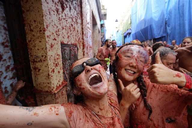 Women react as they throw tomatoes at each other during the annual “Tomatina”, tomato fight fiesta, in the village of Bunol near Valencia, Spain, Wednesday, August 30, 2023. Thousands gather in this eastern Spanish town for the annual street tomato battle that leaves the streets and participants drenched in red pulp from 120,000 kilos of tomatoes. (Photo by Alberto Saiz/AP Photo)