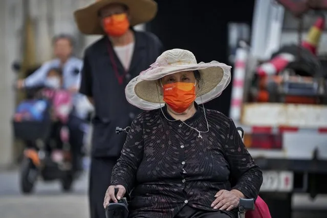 A woman wearing a face mask drives her electric wheelchair followed by her companion on a street in Beijing, Monday, August 29, 2022. (Photo by Andy Wong/AP Photo)
