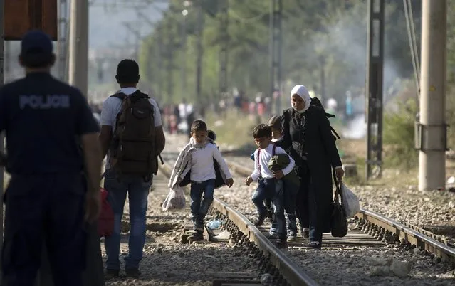 A migrant family tries to cross the Macedonian-Greek border near Gevgelija, Macedonia, as a Greek policeman looks at them, September 5, 2015. (Photo by Stoyan Nenov/Reuters)