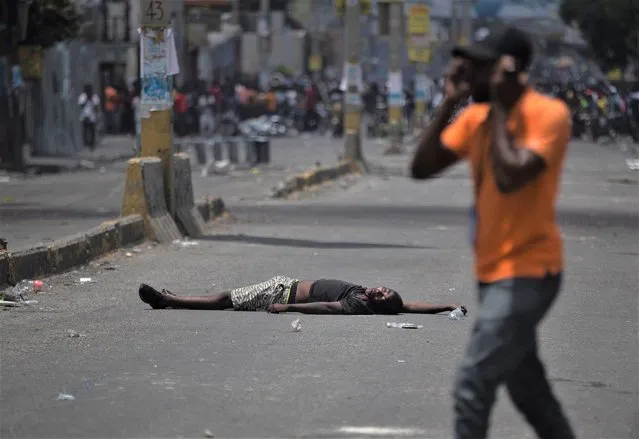 A man walks past the body of a man after he was shot in the head by unknown assailants during a protest in Port-au-Prince, Haiti, Monday, August 22, 2022. (Photo by Odelyn Joseph/AP Photo)