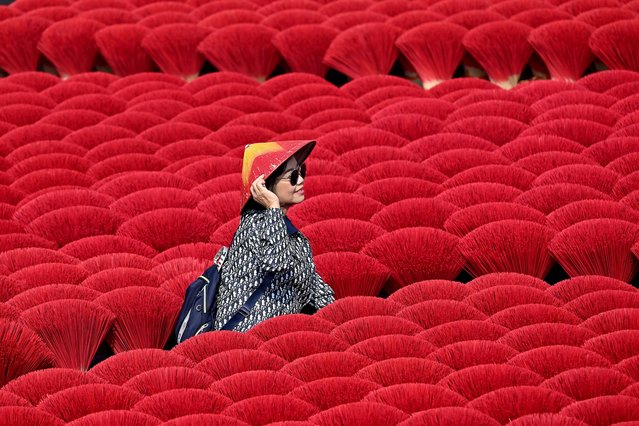 A tourist poses in front of incense sticks drying in a courtyard in Quang Phu Cau village on the outskirts of Hanoi on January 21, 2025, ahead of Lunar New Year celebrations, known in Vietnam as Tet. (Photo by Nhac Nguyen/AFP Photo)