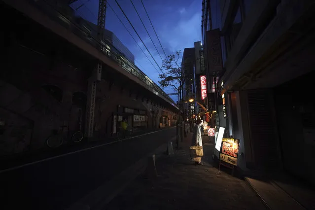 A woman wearing a face mask against the spread of the new coronavirus looks at menu of a restaurant at an empty street in Tokyo Tuesday, April 28, 2020. (Photo by Eugene Hoshiko/AP Photo)