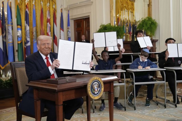 President Donald Trump, left, holds up a signed executive order as young people hold up copies of the executive order they signed at an education event in the East Room of the White House in Washington, Thursday, March 20, 2025. (Photo by Ben Curtis/AP Photo)
