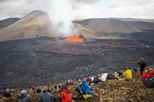 Onlookers watch as lava flows from the vulcano in Fagradalsfjall, Iceland, around 40 kilometres (25 miles) from the capital Reykjavik, on August 10, 2022, following an eruption that has been ongoing since August 3, 2022. The volcano erupted on August 3, some 40 kilometres (25 miles) from Reykjavik, near the site of the Mount Fagradalsfjall volcano that erupted for six months in March-September 2021, mesmerising tourists and spectators who flocked to the scene. (Photo by Jeremie Richard/AFP Photo)