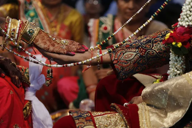 A bride and a groom perform rituals during a mass wedding in Surat, India, Sunday, December 24, 2017. 251 young couples, including five Muslim couple and one Christian couple tied the knot at the mass wedding hosted by Indian diamond trader Mahesh Savani, who has been funding the weddings of fatherless women in the city of Surat for several years. Weddings in India are expensive affairs with the bride's family traditionally expected to pay the groom a large dowry of cash and gifts. Hundreds of people, mostly family members and neighbors of the couple, are hosted at lavish meals over a number of days adding to the costs. (Photo by Ajit Solanki/AP Photo)