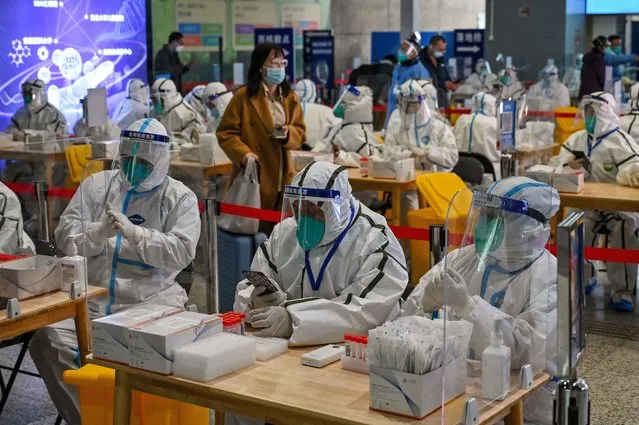 Health workers wait to test passengers for the Covid-19 coronavirus after their arrival at Hongqiao railway station in Shanghai, on December 6, 2022. (Photo by Hector Retamal/AFP Photo)