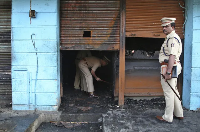 An Indian police official inspects a burnt restaurant in Kalasipalyam district, a busy and congested area in Bangalore, India, Monday, January 8, 2018. A fire in the restaurant early Monday killed five workers who were sleeping inside the building, police said. (Photo by Aijaz Rahi/AP Photo)