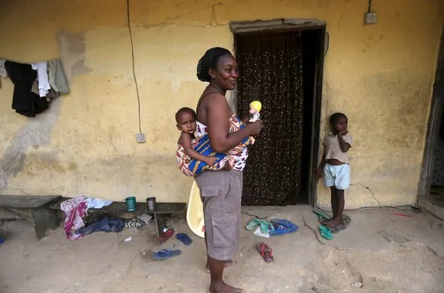 A woman holds a doll as she carries her child on her back in front of her home in Yeneka village on the outskirts of the Bayelsa state capital, Yenagoa, in Nigeria's delta region October 8, 2015. (Photo by Akintunde Akinleye/Reuters)