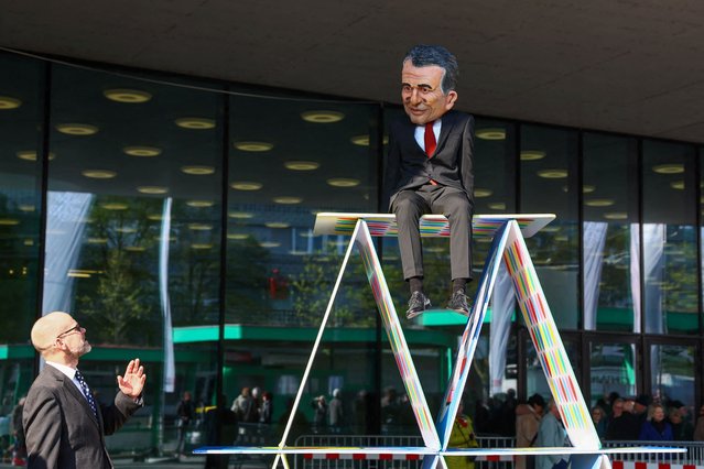 A person wearing a mask depicting CEO of UBS Group Sergio Ermotti sits on top of an house of cards, as climate activists gather in front of St. Jakobshalle where UBS holds its Annual General Meeting, one year after buying rival Swiss bank Credit Suisse, in Basel, Switzerland, on April 24, 2024. (Photo by Denis Balibouse/Reuters)