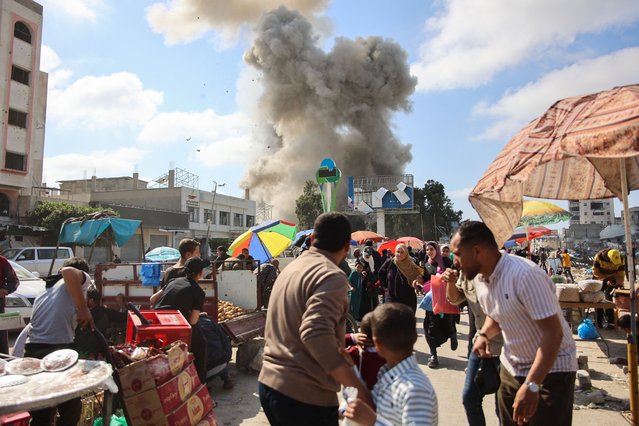Palestinians look at smoke billowing during Israeli bombardment on the Firas market area in Gaza City on April 11, 2024, amid the ongoing conflict between Israel and the Palestinian Hamas group. (Photo by AFP Photo/Stringer)