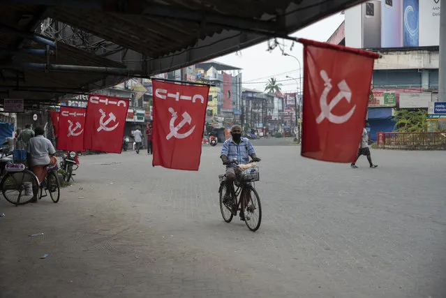 A man wearing mask as a precaution against COVID-19 pedals past flags of a Communist party trade union during a nation wide strike by various trade unions in Kochi, Kerala state, India, Thursday, November 26, 2020. (Photo by R.S. Iyer/AP Photo)