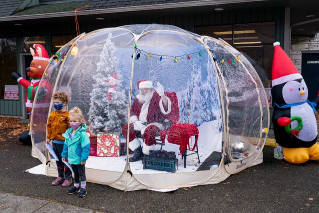Mateo Johnson, 6, and Neah Johnson, 3, pose for a photo with Santa on December 6, 2020 in Seattle, Washington. Known as the Seattle Santa, he is usually booked for private events but is set up this year in a socially-distanced snow globe for public visits during the COVID-19 pandemic. (Photo by David Ryder/Getty Images)