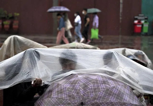 Roadside vendors cover themselves with plastic sheets to protect from monsoon rain in Kathmandu, Nepal, Monday, June 26, 2023. (Photo by Niranjan Shrestha/AP Photo)