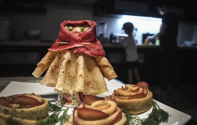 A family cooks a holiday dinner at their apartment as a pancake woman stands on a table in Moscow on March 14, 2021, during celebrations of Maslenitsa, the eastern Slavic Shrovetide. Shrovetide or Maslenitsa is an ancient farewell ceremony to winter, traditionally celebrated in Belarus, Russia and Ukraine including pancake cooking as a part of the ceremony. (Photo by Alexander Nemenov/AFP Photo)