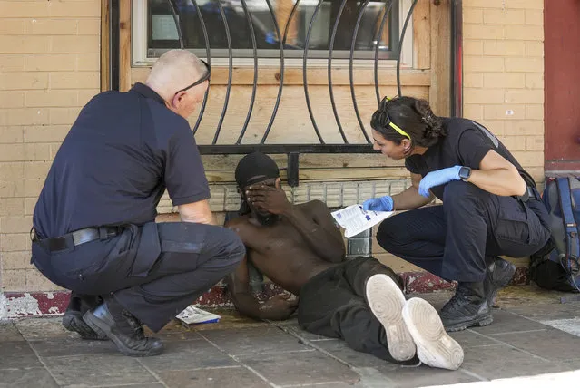Austin-Travis County Emergency Medical Services medic Capt. Darren Noak, left, and M. Megally check on a man on East 6th Street in Austin, Texas, on Wednesday July 12, 2023, during an excessive heat warning when the temperature reached up to 107 degrees. Then man was transported by ambulance to a hospital for heat-related issues. (Photo by Jay Janner/Austin American-Statesman via AP Photo)
