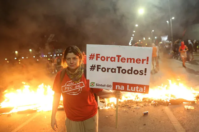 A demonstrator holds a banner which reads “Out Temer!” “Out everyone!” in front of burning barricades during a protest against a constitutional amendment, known as PEC 55, that limit public spending, in front of Brazil's National Congress in Brasilia, Brazil, November 29, 2016. (Photo by Adriano Machado/Reuters)