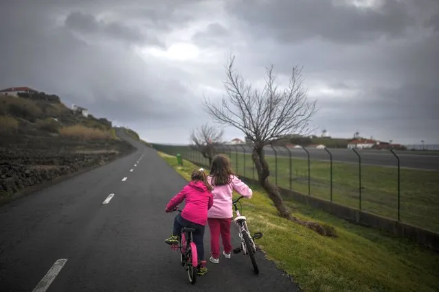 Two girls ride their bicycles on a road alongside the Corvo Airpot in Vila do Corvo in Azores on March 10, 2021. With occasional shortages of petrol and fruit, Corvo is no stranger to the pitfalls of isolation – but its remoteness has had one major advantage: the smallest island of the Azores archipelago off the Portuguese coast has been spared from the pandemic sweeping the rest of the globe. (Photo by Patricia De Melo Moreira/AFP Photo)