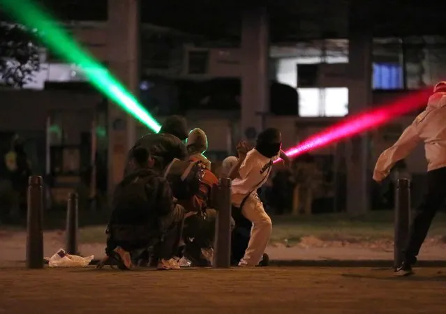 Laser beams are shot through the air as demonstrators hurl rocks during a protest demanding government action to tackle poverty, police violence and inequalities in healthcare and education systems, in Bogota, Colombia, May 10, 2021. (Photo by Luisa Gonzalez/Reuters)